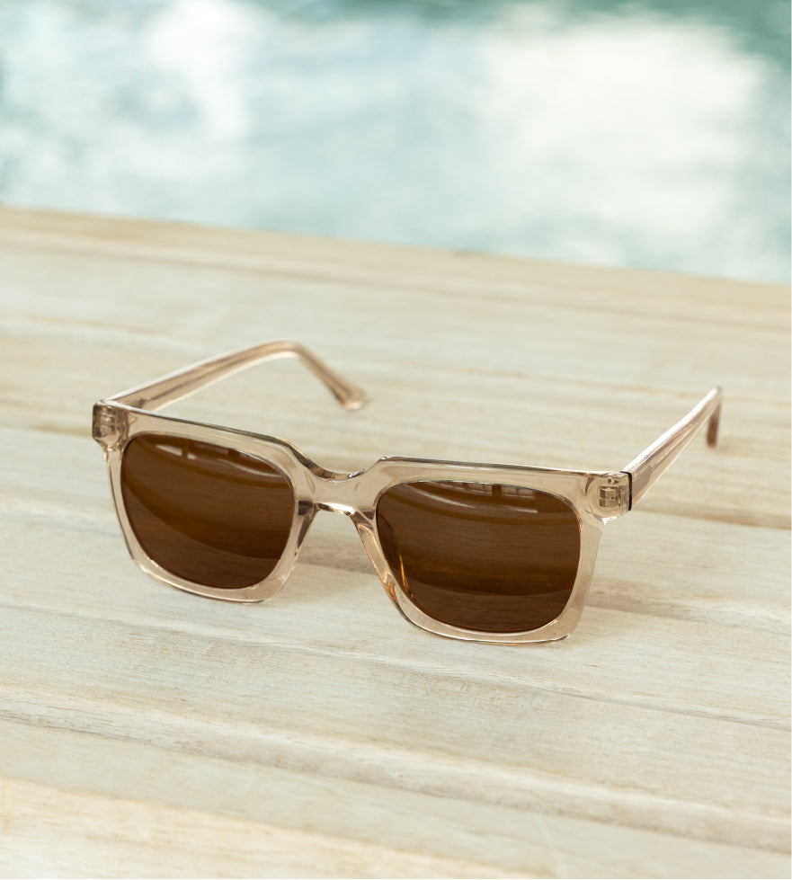 Rectangular sunglasses with clear frames and brown lenses on a wooden surface.