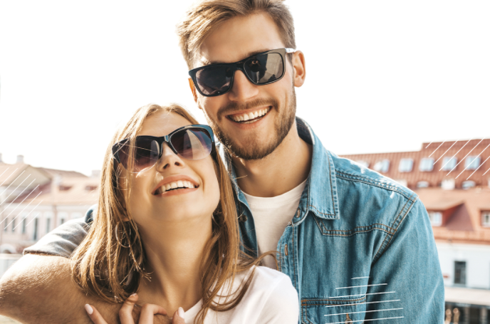 Foto de una pareja joven que trae puestos unos lentes de sol mientras disfruta de un paseo.