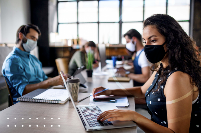 Mujeres y hombres con cubrebocas se encuentran concentrados mientras trabajan en sus computadoras