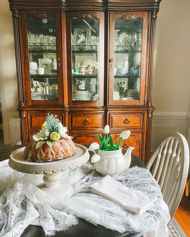 Faux cake on table with linens and china hutch behind