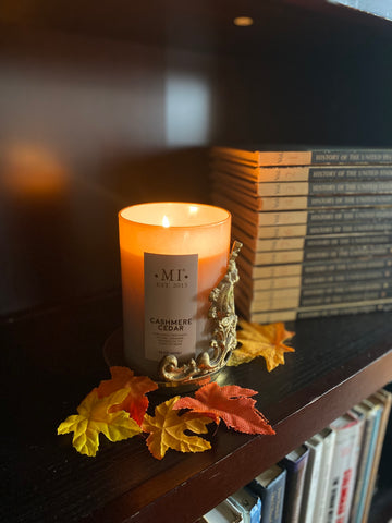 Colonial Candle Cashmere Cedar Candle burning in a gold scroll holder beside a stack of antique books