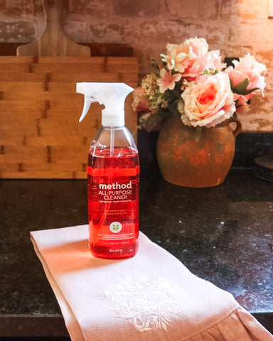 Method Honey Crisp Apple Cleaning spray on pink damask linen towel with cutting boards and flowers behind
