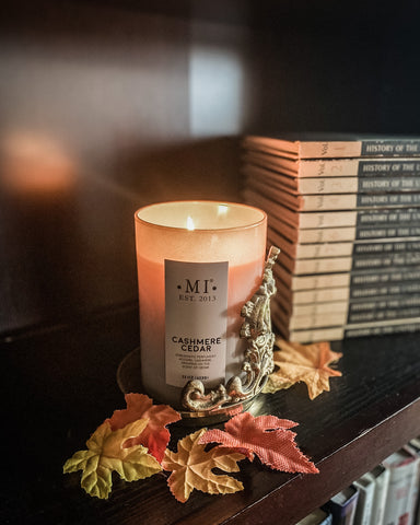 cashmere cedar candle flickering with autumn leaves around and antique books stacked behind