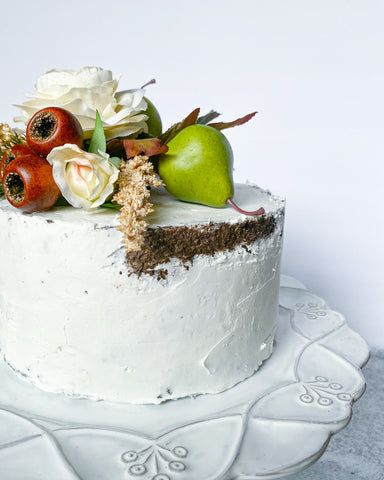 chocolate faux cake with white silk flowers artificial pears around on white cake stand