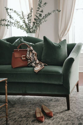 green velvet sofa with brown handbag sitting upright on it and brown shoes under