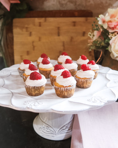 raspberry mojito cupcakes on white cake stand with wooden cutting boards behind and pink flowers in a brown ceramic vase