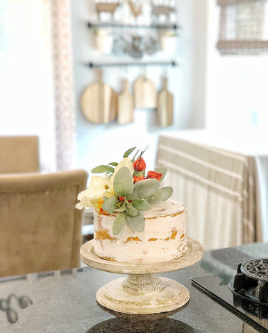 faux cake with orange flowers and greenery on kitchen counter with wooden boards on wall behind