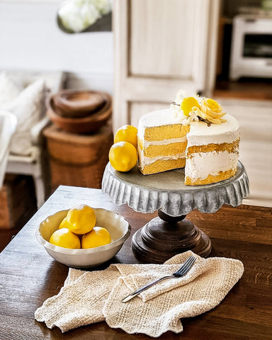 faux lemon cake on rustic metal cake stand with lemons surrounding