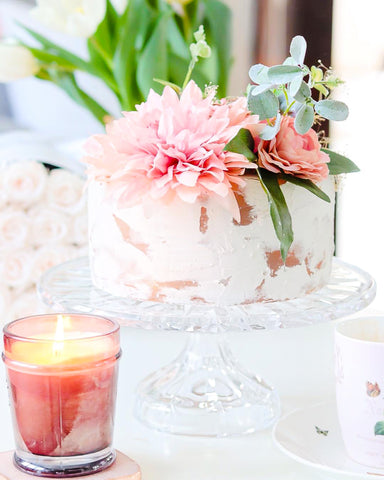 faux cake with pink dahlia and greenery and pink glowing candle in front