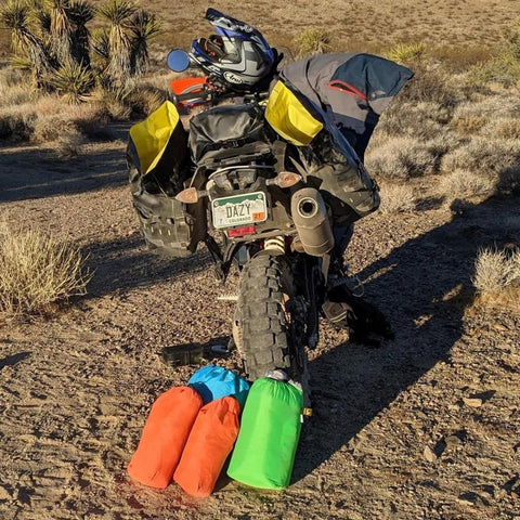 Multiple luggage bags on and beside motorcycle at a desert site