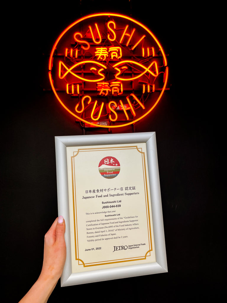 JETRO certificate framed, held below a neon orange light up SushiSushi Logo