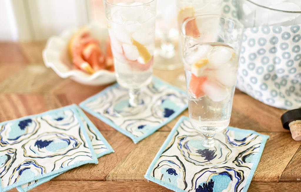 Fizzy cocktail in a clear glass with grapefruit garnish on an oyster print cocktail napkin