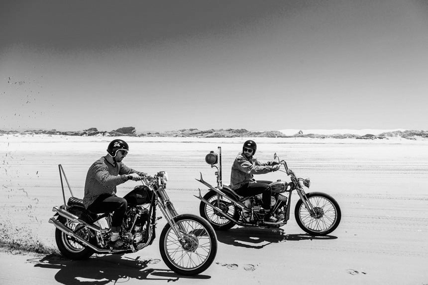 Two men riding motorbikes on the beach