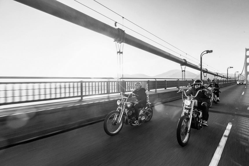 Three men riding motorbikes across a bridge