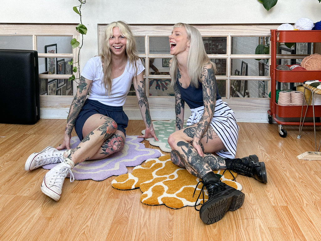 Twin sisters Victoria and Charlotte Brumwell sitting on the floor together laughing at tattoo studio crooked finger located in Halifax Nova Scotia 