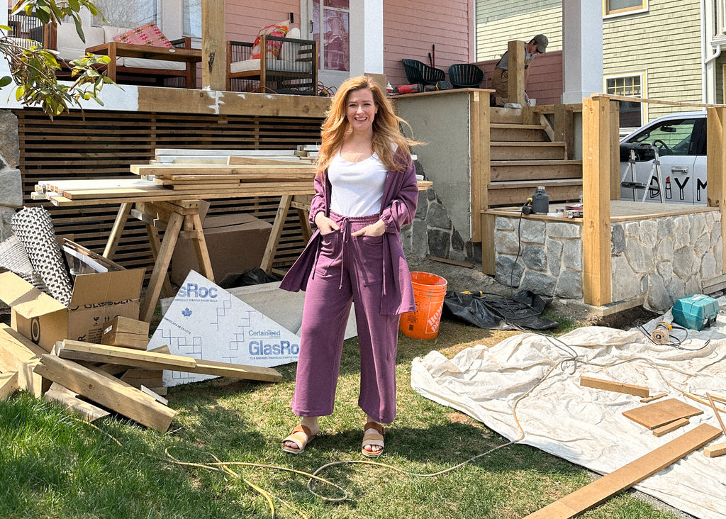 Rebekah standing in the front of her home while it is under construction with the deck and stairs into the front deck are unfinished
