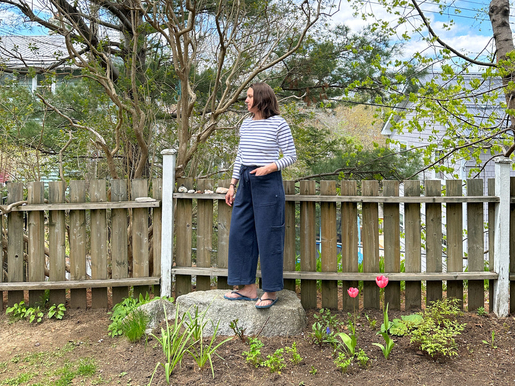 a photo of Laura standing on a rock in her backyard with a fence behind her and tulips blooming in the garden 