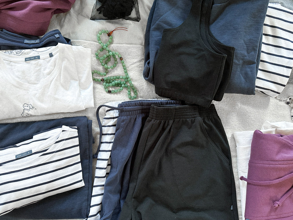 Packing and getting ready for a trip by organizing different piles of Ana + Zac clothing on a bed with Jade mala beads 