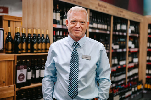 Male liquor store manager wearing a blue button down dress shirt, standing in aisle