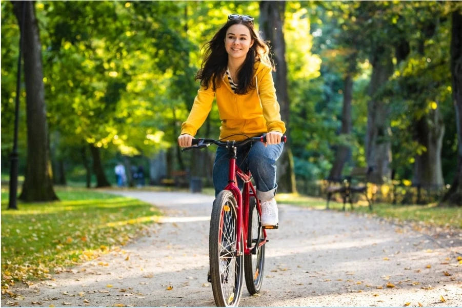 A woman in a yellow hoodie rides a red bicycle on a park path.