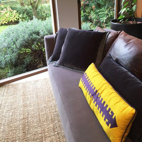 Bahceye bakan gri kanepede fume kadife ve sari ustune mor hayat agaci desenli yastiklar_Dark grey velvet cushions and yellow silk pillow with purple tree of life motif on a sofa facing the garden