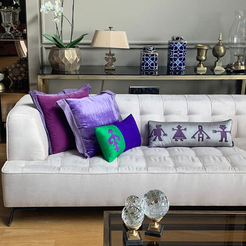 Ev aksesuarli dresuarin onundeki beyaz kanepede mor yesil gri tonlarinda kadife ve ipek kirlentler_Velvet and silk throw pillows in purple green and gray tones on the white sofa in front of the home accessory dresser