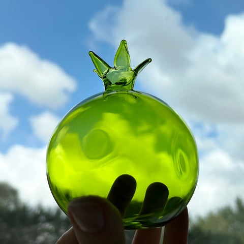 Fonda gokyuzu ve elde yesil seffaf cam nar_Green transparent glass pomegranate in a hand and sky in the background