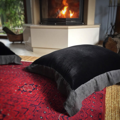 Sominenin onundeki bordo Afgan halisinin ustunde siyah ipek kadife yer minderi_Black silk velvet floor cushion on a dark red Afghan carpet in front of the fireplace