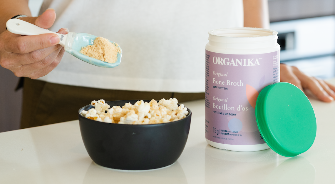 A bowl of popcorn on a kitchen counter beside Organika's Beef Bone Broth