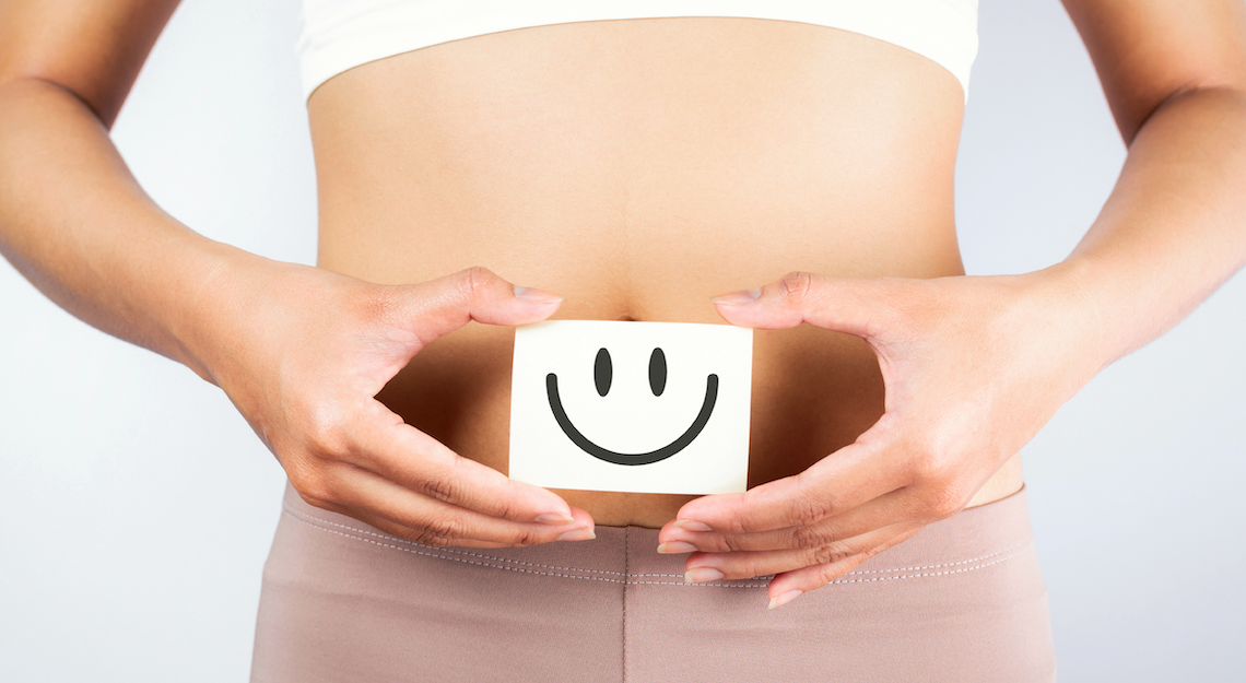 Femme tenant un smiley devant son estomac pour signifier qu'elle a des intestins sains.