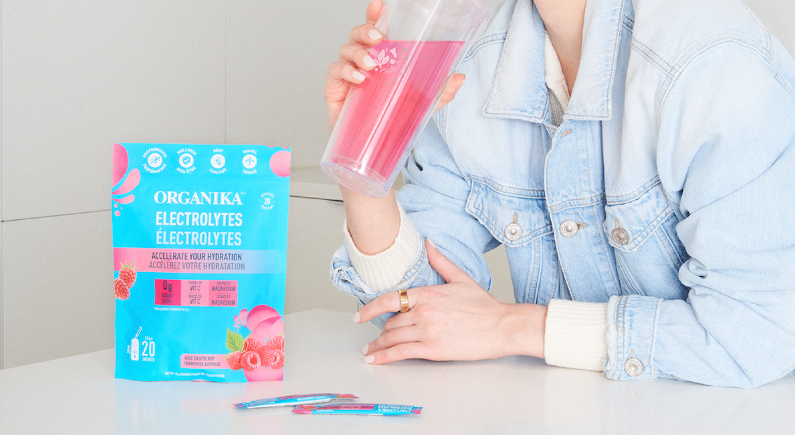 Organika's Electrolytes Sachets on a table with a woman drinking from a tumbler
