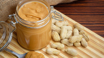A jar of peanut butter surrounded by peanuts