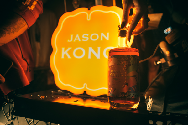 A neon sign with Jason Kong Gin logo and a bottle being closed by woman hands