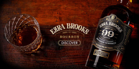 Bottle of Ezra Brooks Whiskey lay down on a wooden table with a glass of whisky on a side