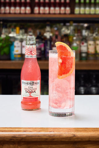 Fever-Tree Pink Grapefruit Soda bottle and a served glass with ice and orange slice on a bar counter