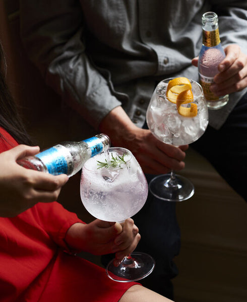 Fever-Tree being poured on rosemary and orange peel garnished glasses in hands of people