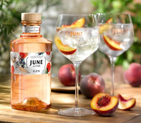 June Peach by G Vine bottle with 2 glasses of Gin Tonic and pieces of peach on a garden table