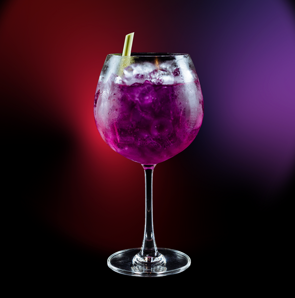 a glass of Gin Tonic with a blue purple twist made with Jason Kong Gin on a colored background
