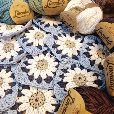 Many crochet squares with a white flower, a dark blue petal and then a light blue outside. 