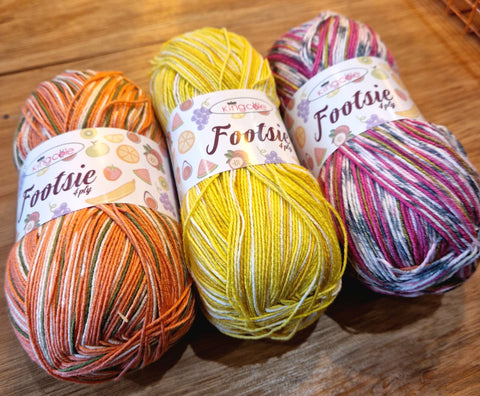 Three multicoloured balls of yarn lined up in a row, one mainly orange, one mainly yellow, and one mainly pink. The ball band says "Footsie 4ply".