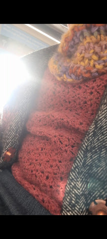 A selfie of a person wearing a red crochet jumper, a multi coloured, orange-y/purple-y cowl and a grey coat. You can't see a face, body or make out who it is. 