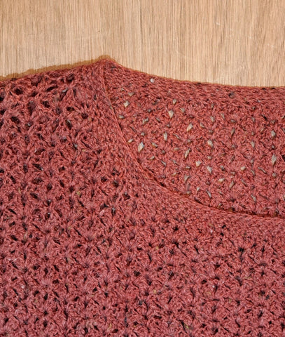 A close up of half of the neckline of a red, crocheted jumper. 