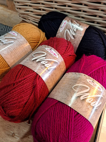 Four balls of King Cole Wool Aran laid on a table - colours are mustard, red, magenta and deep, deep navy. 