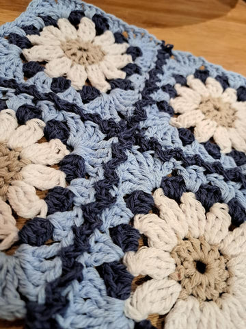 Four granny squares in shades of blue, cream and beige crocheted together with a dark blue colour in a slightly open way. 