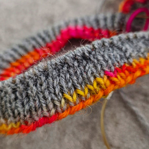 A swatch of stocking stitch in grey and orange-y colours on circular needles.