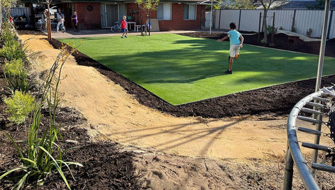 Neu gestalteter Garten mit einem großen Platz mit grünem Rasen und einem Fahrrad-Pumptrack, der um den gesamten Hof verläuft.