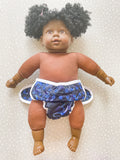 A dark skined doll wearing a modern preflat cloth nappy with a dinosaur cover