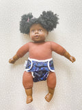 A dark skined doll wearing a modern preflat cloth nappy with a dinosaur cover