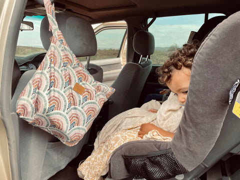 small child with curly brown hair in car seat with a cloth bums wet bag 