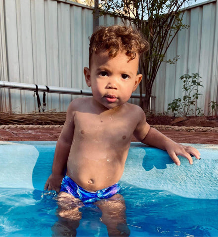 little curly haired boy wearing a blue reusable swim nappy